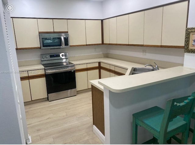 kitchen featuring sink, stainless steel appliances, kitchen peninsula, light hardwood / wood-style floors, and cream cabinetry