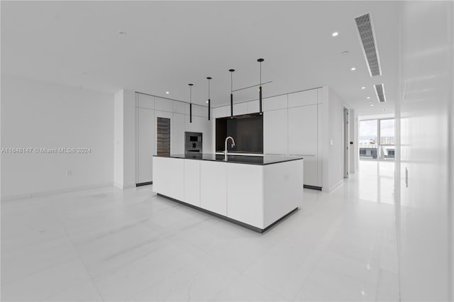 kitchen featuring white cabinets, black microwave, sink, pendant lighting, and a kitchen island with sink