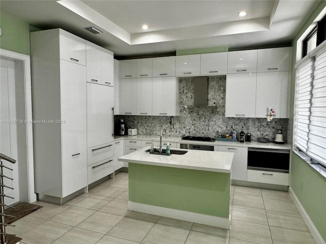 kitchen featuring a wealth of natural light, sink, wall chimney range hood, and an island with sink