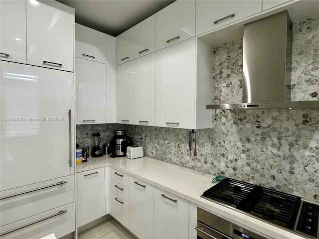 kitchen with wall chimney range hood, built in fridge, white cabinetry, and light tile patterned floors