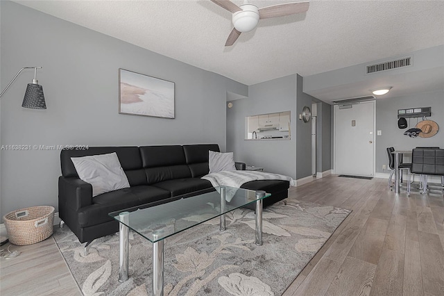 living room with ceiling fan, a textured ceiling, and light hardwood / wood-style flooring