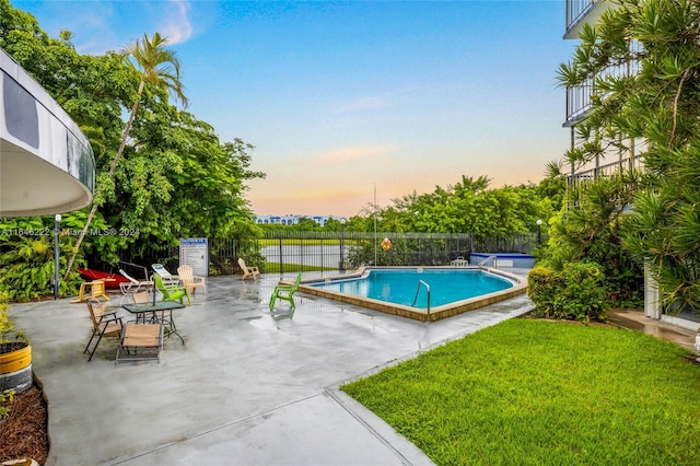 pool at dusk with a patio and a yard