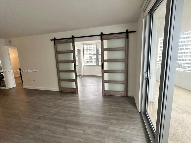 unfurnished room featuring a barn door, dark wood-type flooring, and a healthy amount of sunlight