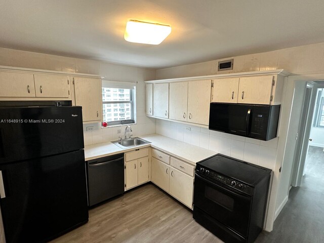 kitchen featuring sink, hardwood / wood-style flooring, black appliances, and tasteful backsplash