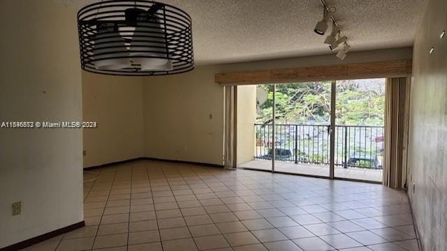 unfurnished room featuring a textured ceiling, light tile patterned floors, and rail lighting