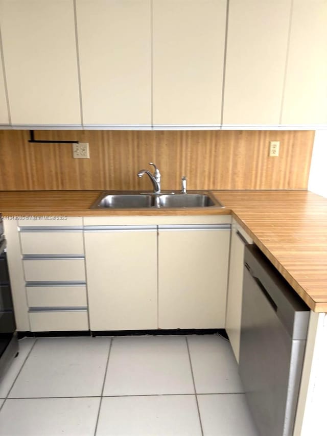 kitchen featuring stainless steel dishwasher, a sink, light countertops, light tile patterned flooring, and white cabinetry