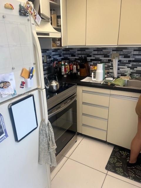 kitchen featuring stainless steel electric range oven, tasteful backsplash, light tile patterned floors, and white refrigerator