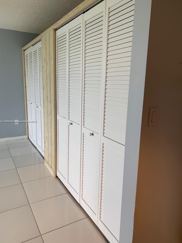 corridor featuring light tile patterned flooring, a textured ceiling, and baseboards
