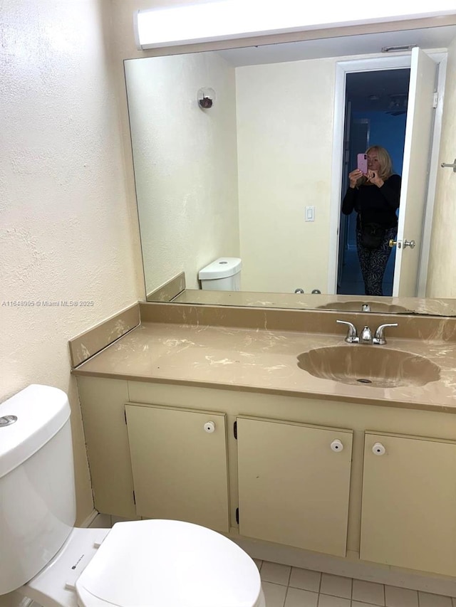 half bath featuring toilet, vanity, tile patterned flooring, and a textured wall