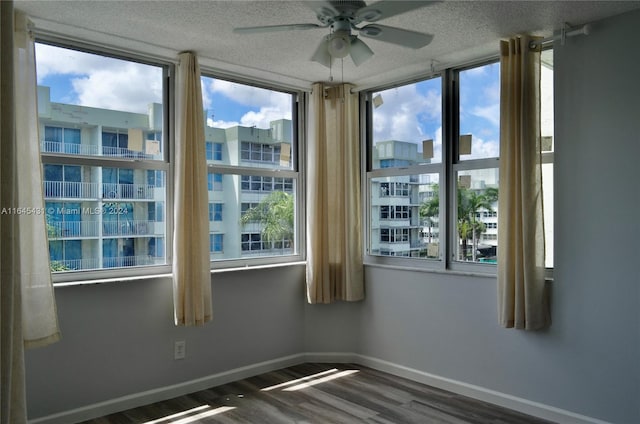 empty room with a textured ceiling, ceiling fan, plenty of natural light, and dark hardwood / wood-style flooring