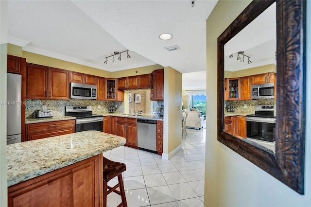 kitchen with crown molding, appliances with stainless steel finishes, light tile patterned floors, and light stone countertops