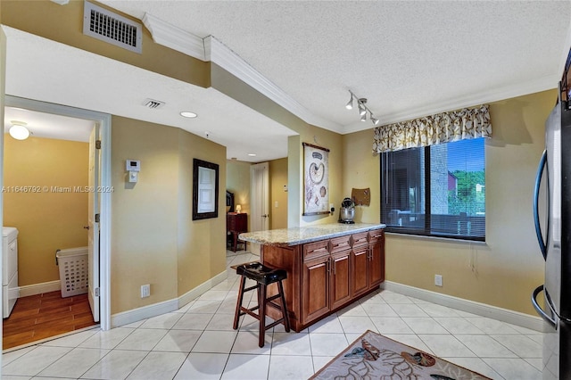 kitchen featuring a textured ceiling, a breakfast bar area, washing machine and clothes dryer, kitchen peninsula, and light tile patterned flooring