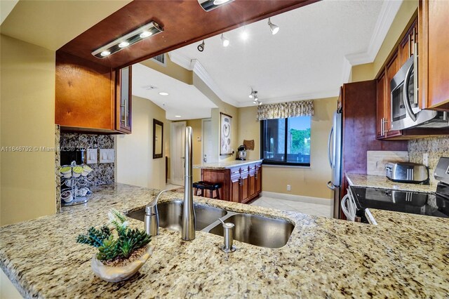 kitchen with backsplash, crown molding, appliances with stainless steel finishes, light stone counters, and kitchen peninsula