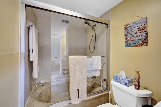 bathroom featuring a shower with door and toilet