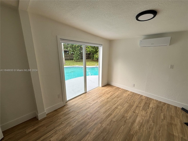 empty room featuring vaulted ceiling, wood-type flooring, a textured ceiling, and a wall unit AC