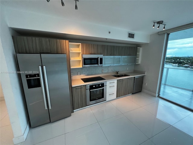 kitchen featuring backsplash, sink, appliances with stainless steel finishes, rail lighting, and light tile patterned floors