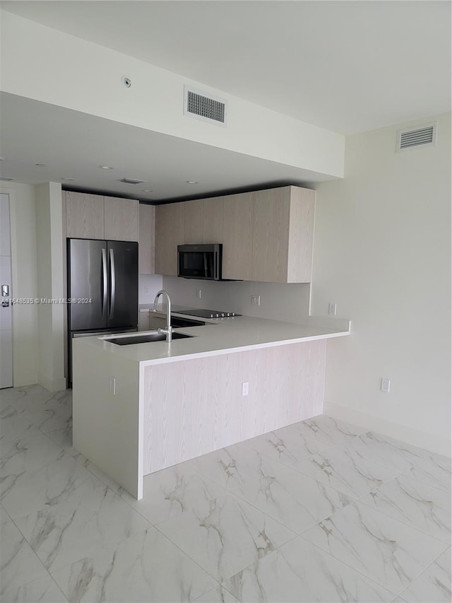 kitchen with appliances with stainless steel finishes, kitchen peninsula, light brown cabinetry, and sink