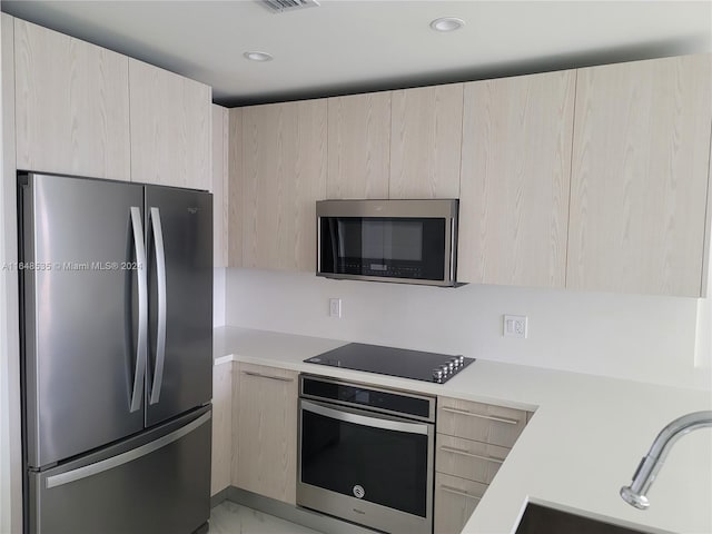 kitchen with light brown cabinetry, stainless steel appliances, and sink