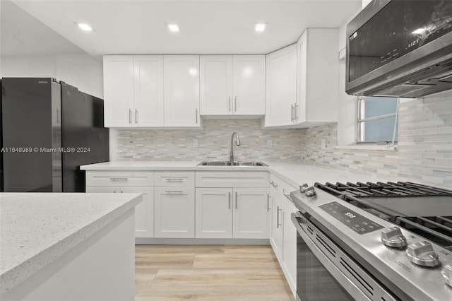 kitchen with sink, tasteful backsplash, light hardwood / wood-style floors, white cabinets, and appliances with stainless steel finishes