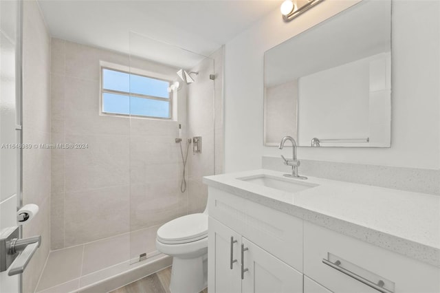 bathroom featuring toilet, vanity, wood-type flooring, and tiled shower