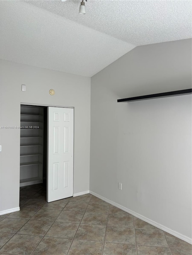 unfurnished bedroom featuring tile patterned floors, a closet, a textured ceiling, and lofted ceiling