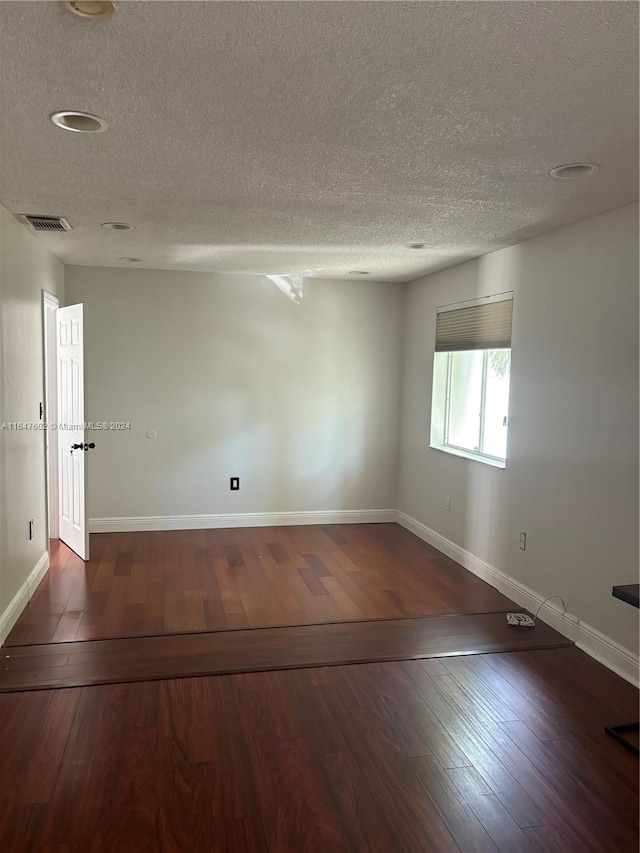 empty room with dark hardwood / wood-style flooring and a textured ceiling