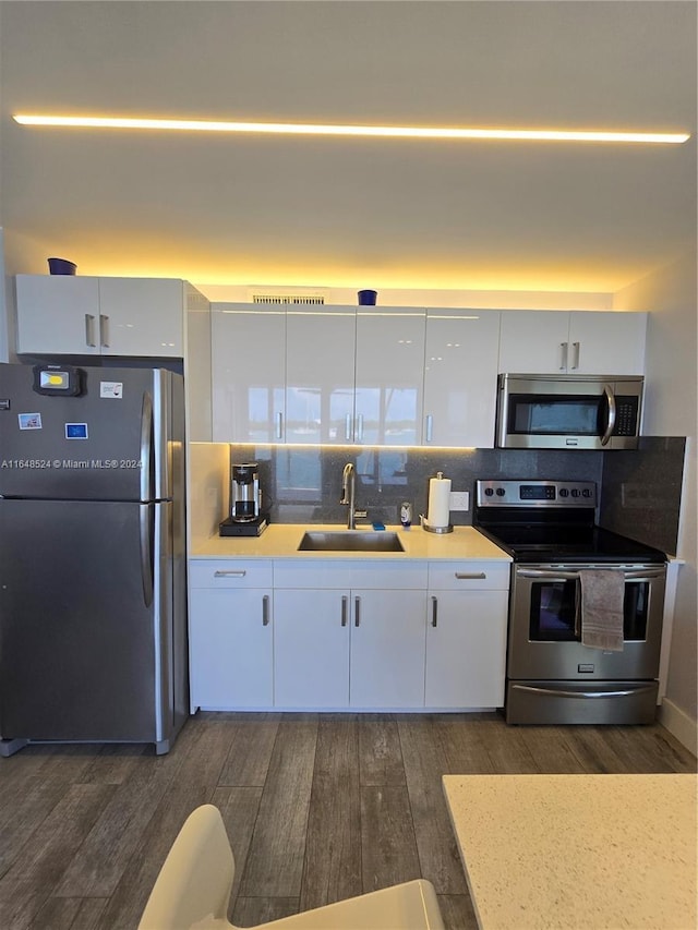 kitchen featuring stainless steel appliances, a sink, white cabinetry, light countertops, and dark wood finished floors