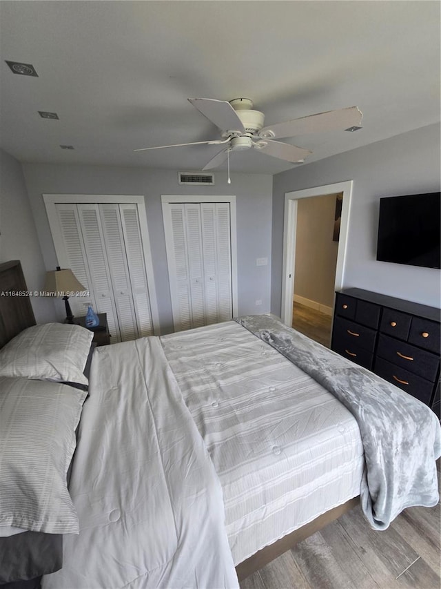 bedroom with multiple closets, visible vents, ceiling fan, and wood finished floors