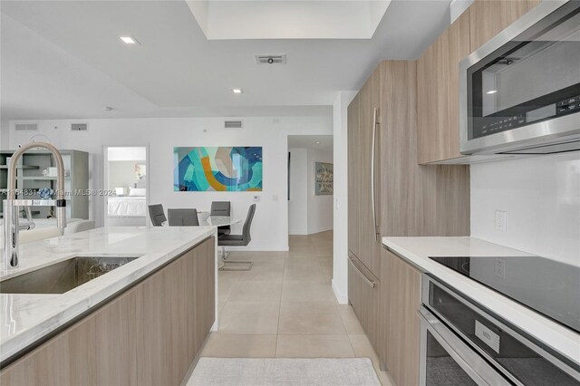 kitchen with light tile patterned floors, appliances with stainless steel finishes, light stone counters, sink, and light brown cabinets