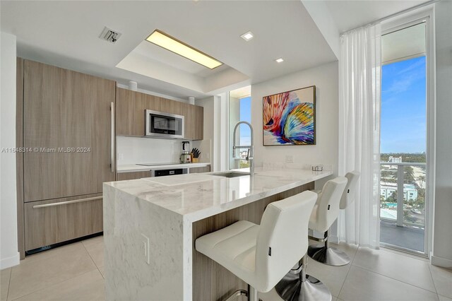 kitchen featuring a kitchen breakfast bar, light stone countertops, sink, stainless steel microwave, and light tile patterned flooring