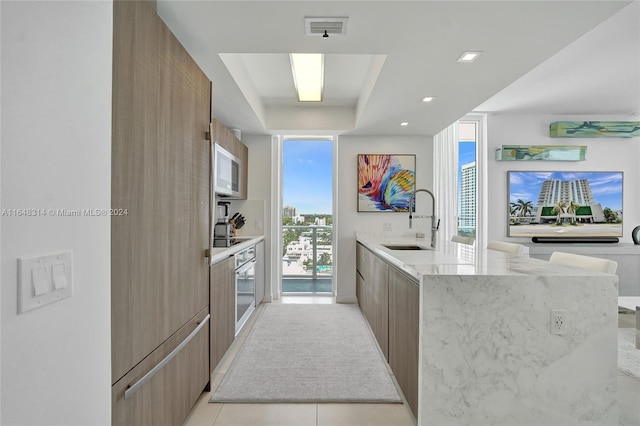 kitchen featuring light tile patterned floors, light stone counters, kitchen peninsula, sink, and stainless steel oven