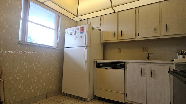 kitchen featuring cream cabinets, light tile patterned flooring, dishwasher, and white refrigerator