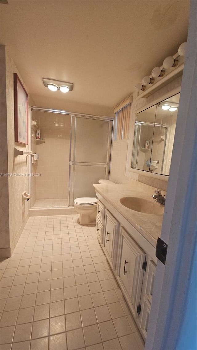 bathroom featuring tile patterned flooring, a shower with door, vanity, and toilet