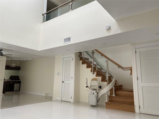 stairway with a towering ceiling, tile patterned flooring, and ceiling fan