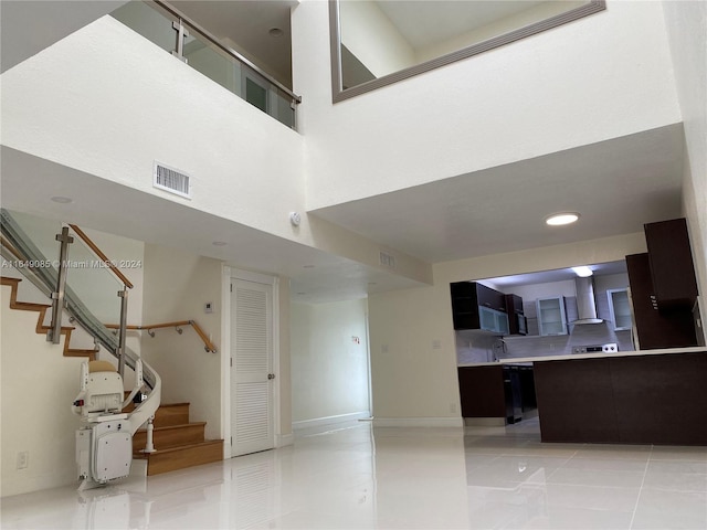 interior space with dishwasher, light tile patterned floors, wall chimney exhaust hood, and a towering ceiling