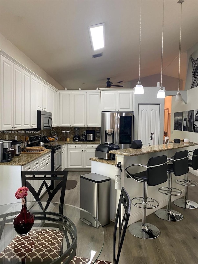 kitchen featuring lofted ceiling, white cabinets, a kitchen island, stainless steel appliances, and decorative light fixtures