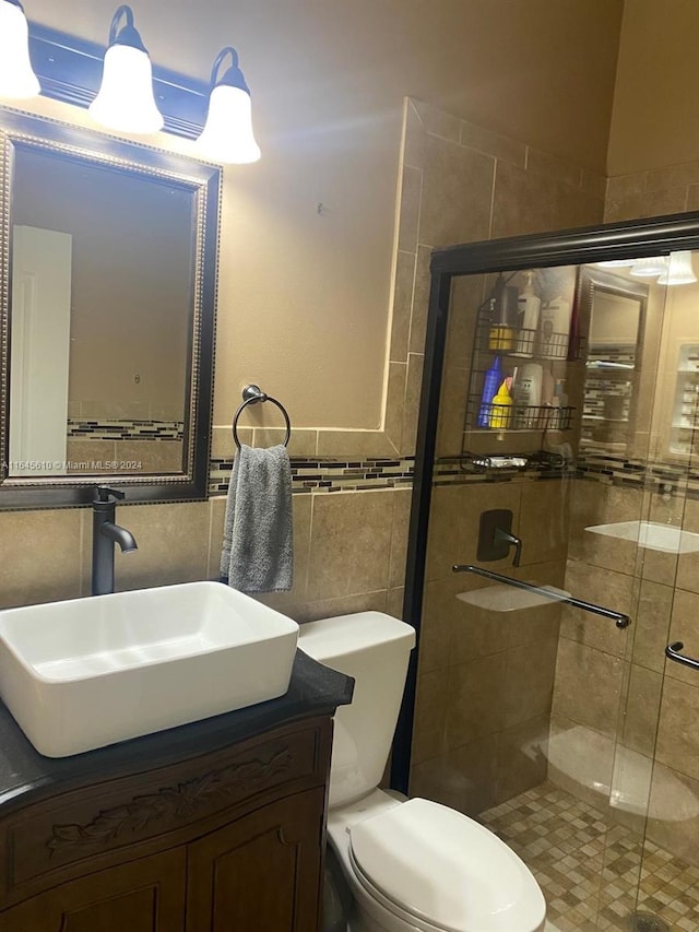 bathroom with toilet, a shower with shower door, vanity, and tile walls