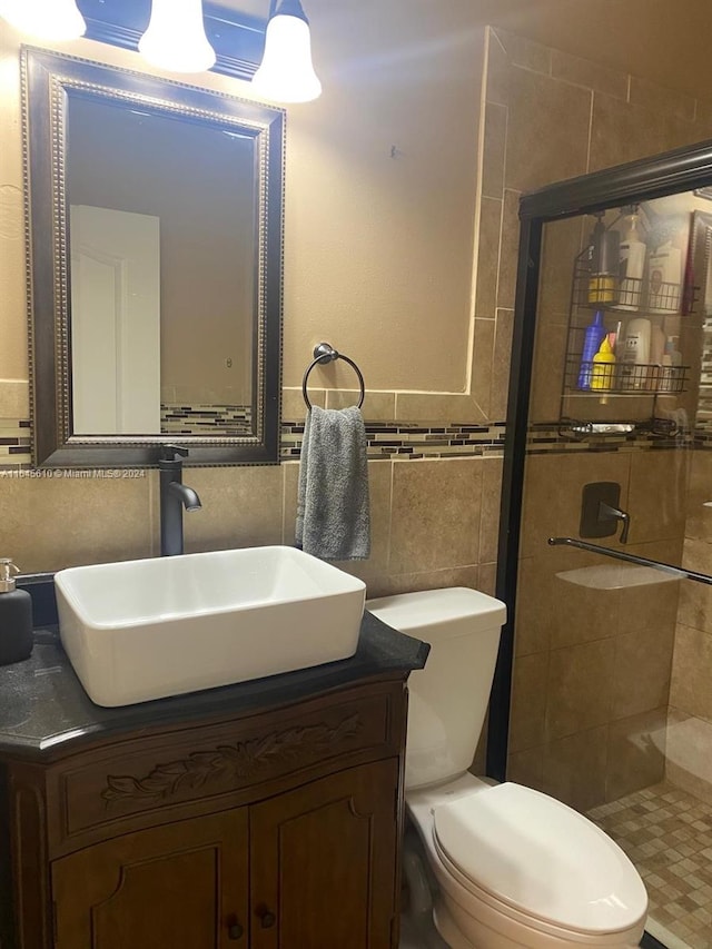 bathroom with toilet, a shower with shower door, vanity, and tile walls