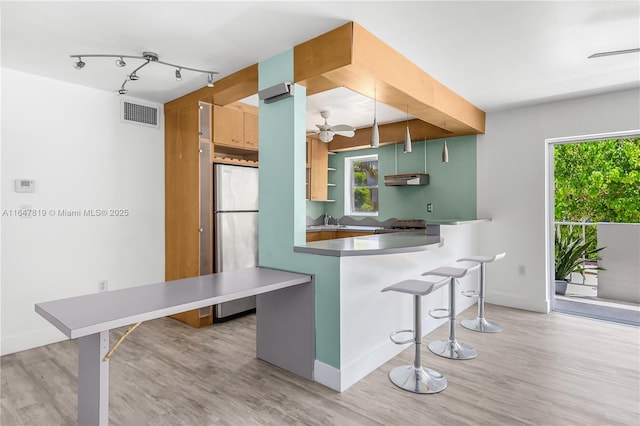 kitchen featuring sink, stainless steel fridge, a kitchen breakfast bar, kitchen peninsula, and light hardwood / wood-style flooring