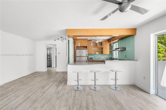 kitchen with ceiling fan, appliances with stainless steel finishes, light hardwood / wood-style floors, a kitchen bar, and kitchen peninsula