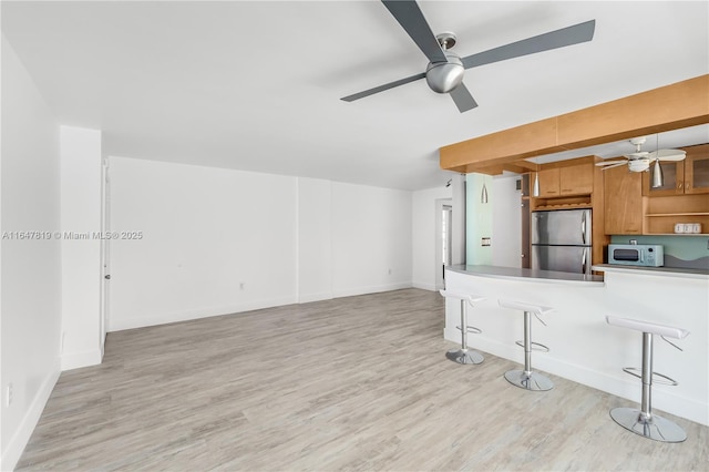 kitchen featuring stainless steel refrigerator, a kitchen bar, kitchen peninsula, and light wood-type flooring