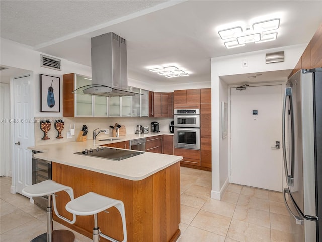 kitchen with kitchen peninsula, a kitchen bar, island exhaust hood, stainless steel appliances, and light tile patterned floors