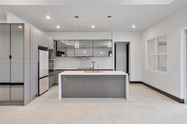 kitchen with oven, decorative light fixtures, refrigerator, an island with sink, and gray cabinets