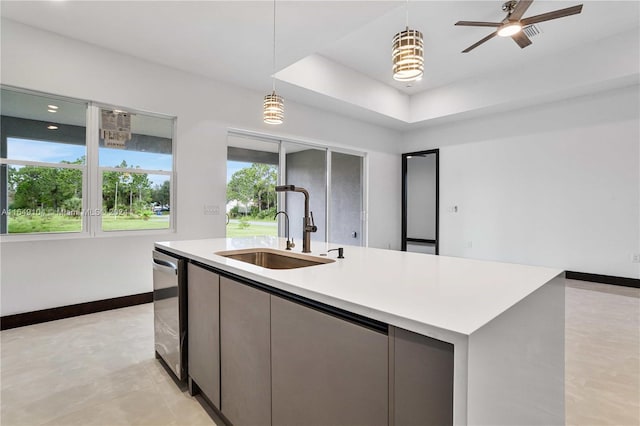 kitchen featuring a center island with sink, ceiling fan, pendant lighting, a tray ceiling, and sink