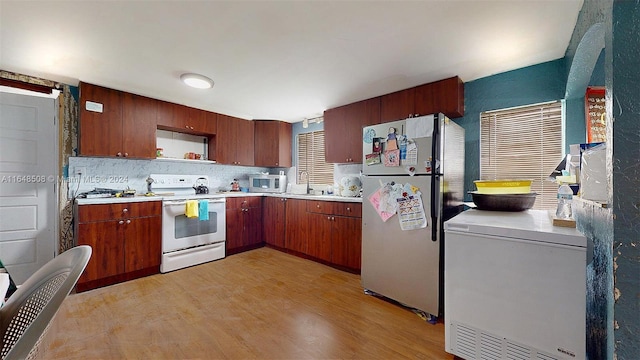 kitchen with decorative backsplash, light wood-type flooring, white appliances, and sink