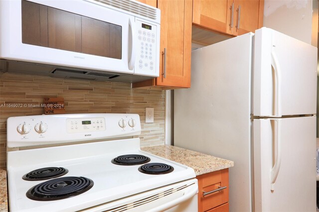 kitchen featuring decorative backsplash, light stone countertops, and white appliances