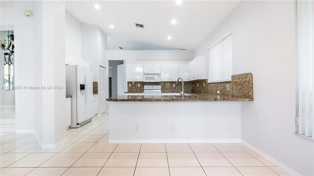 kitchen featuring white appliances, backsplash, white cabinets, kitchen peninsula, and dark stone counters