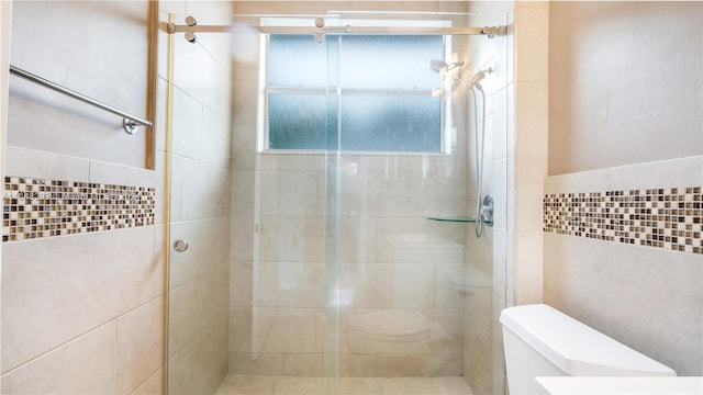 bathroom with tile walls, toilet, and a shower with shower door