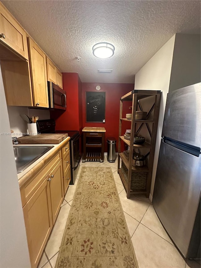 kitchen with appliances with stainless steel finishes, light tile patterned flooring, a textured ceiling, and sink