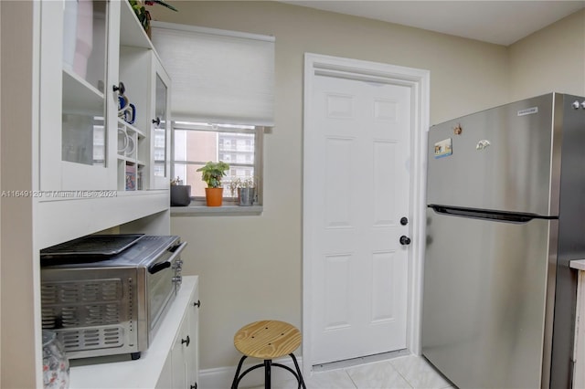 kitchen with stainless steel refrigerator, white cabinets, and light tile patterned floors